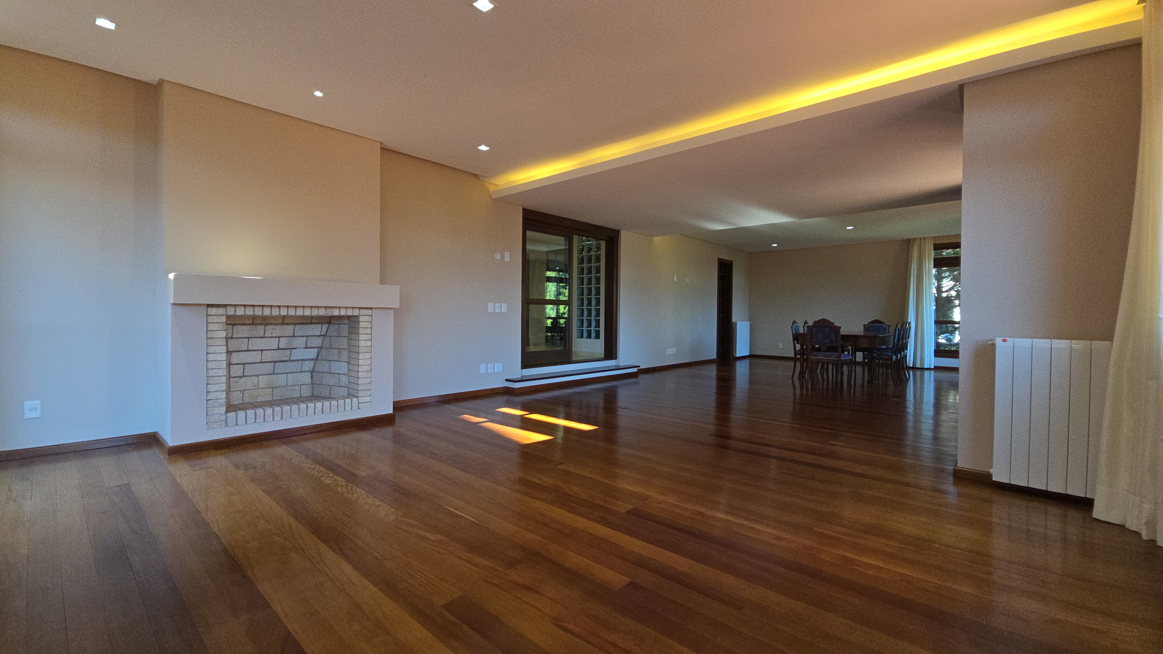 Living grandioso da Mansão La Guapa com lareira de tijolos, piso de madeira e sala de jantar ao fundo